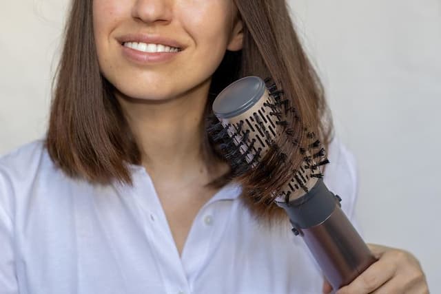 Ung kvinde styler sit brune hår med varmluftbørste