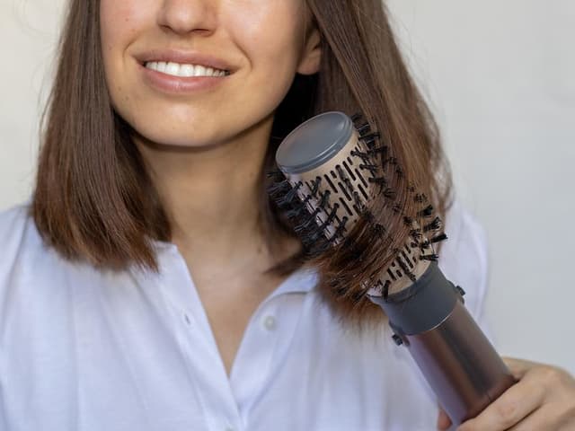 Ung kvinde styler sit brune hår med varmluftbørste