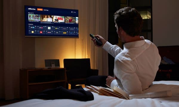 Mann på hotellrom som skrur på TV-en fra sengen
