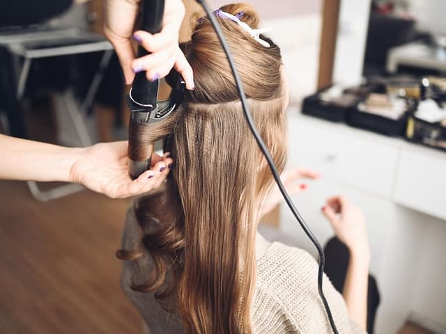 Hair stylist making curls in the hair of a woman with a curling iron in beauty salon
