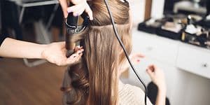 Hair stylist making curls in the hair of a woman with a curling iron in beauty salon