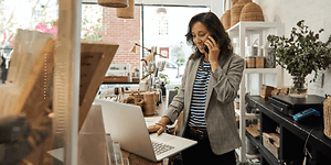 B2B - Elkjøp Control - A woman speaking on her smartphone in front of her laptop in a shop