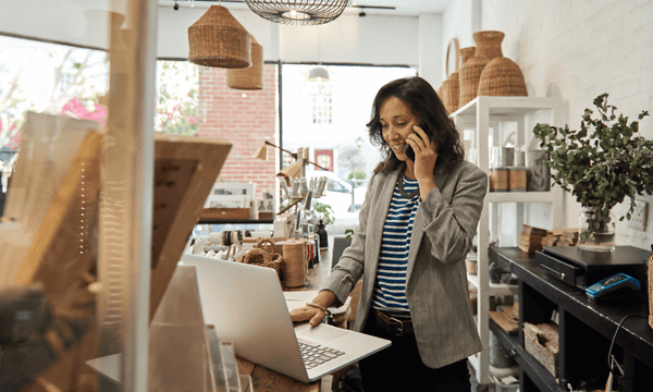 B2B - Elkjøp Control - A woman speaking on her smartphone in front of her laptop in a shop