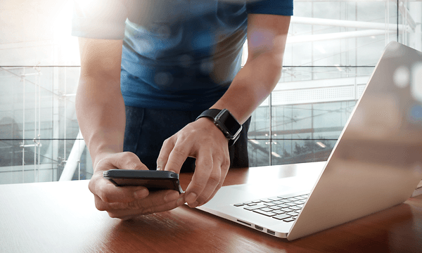 B2B - Android Zero-Touch - A man with his phone in front of his laptop in an office