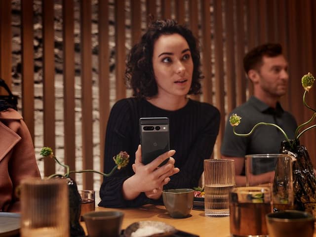 Kvinde sidder på en resturant med sin Google Pixel 7 i hånden