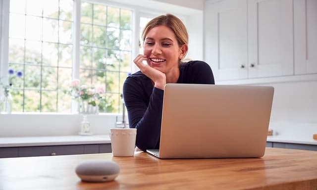 Google - Google Assistant - Woman in kitchen using smart speaker and laptop