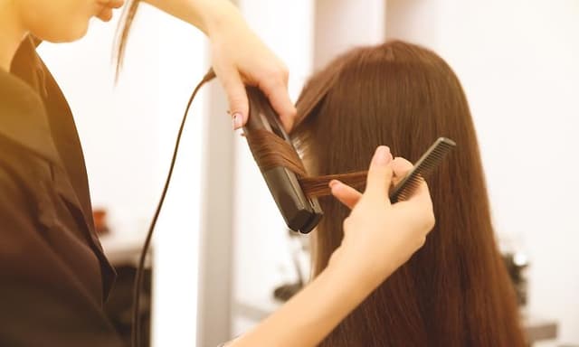 Kvinde med langt brunt hår bliver stylet i salon med glattejern