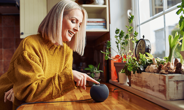 Välj smart högtalare: kvinna som ler och rör vid en rund smart högtalare.