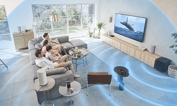 En familj i en soffa i ett stort vardagsrum som tittar på TV och där illustrerade ljudvågor kommer ur en subwoofer