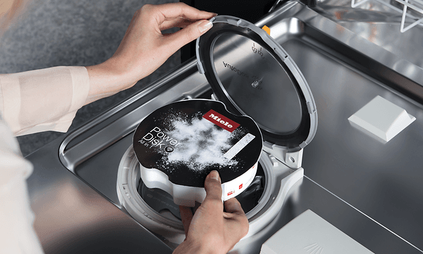 Hender åpner det automatiske doseringssystemet på en Miele oppvaskmaskin