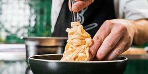 kok i færd med at arrangere pasta i en dyb tallerken