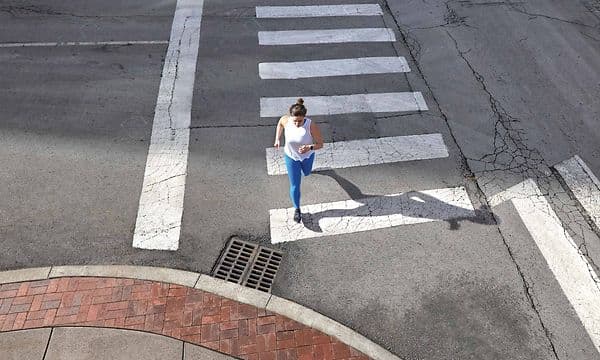 En kvinne som jogger over et fotgjengerfelt med en Garmin Forerunner sportsklokke på armen