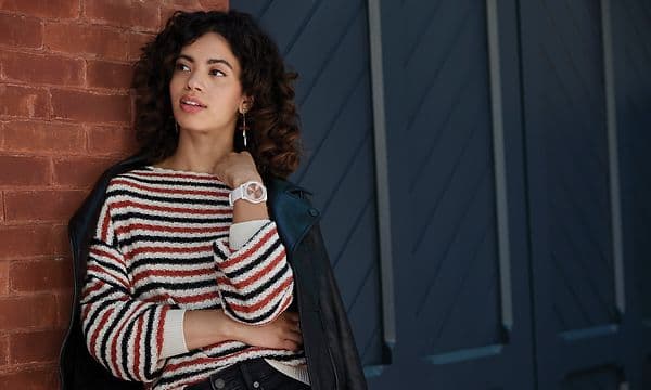 Kvinne lener seg mot en murvegg med en Garmin Vivosmart smartklokke på håndleddet