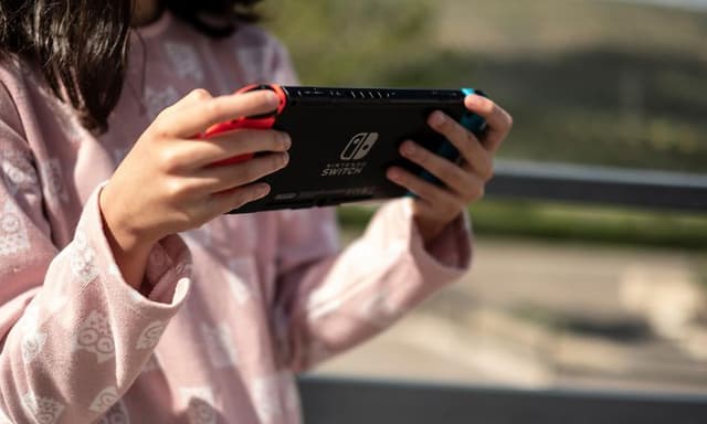 Kouluikäinen tyttö pitelee Nintendo Switch -konsolia kädessään ja pelaa sillä