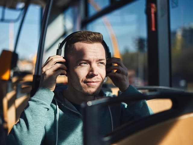 Mies bussissa laittaa kuulokkeita korvilleen