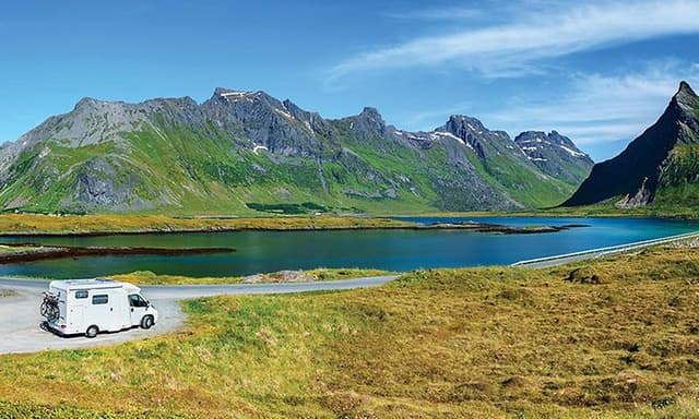 Billede af en autocamper foran en sø og bjerge