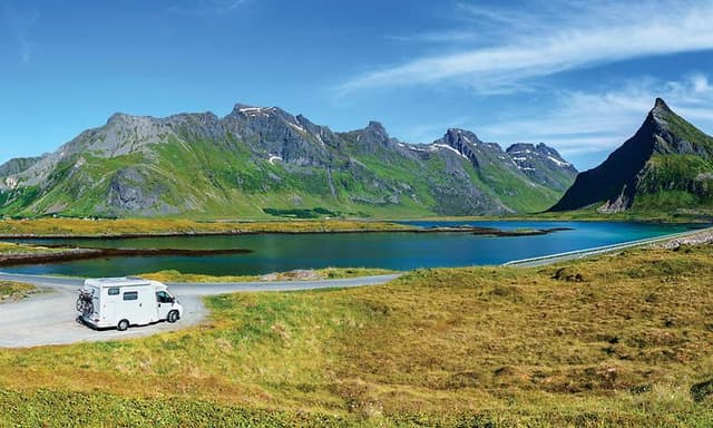 Autocamper parkeret foran en sø og bjerge