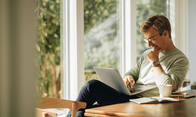 Hymyilevä mies istuu kannettavan edessä