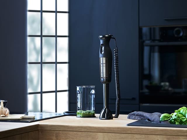 Bosch stavmixer på ett bord bredvid vitlök, lime och basilikablad