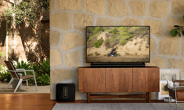 Sort Sonos Arc under en TV og Sonos Sub ved siden av TV-benk i en stue