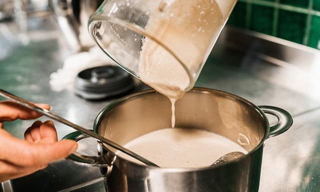 En person häller grönsakssoppa från en blender över i en gryta på en diskbänk av metall