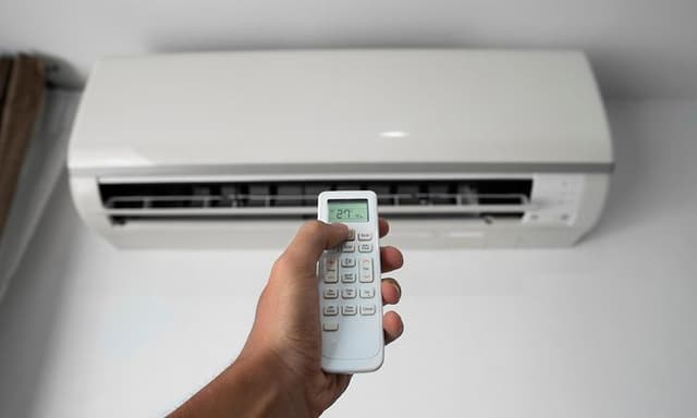 Mies osoittaa ilmalämpöpumppua kaukosäätimellä