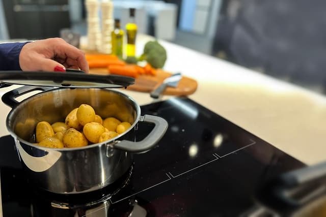 Kvinnas hand som lägger lock på en kastrull med potatis som står på en induktionshäll
