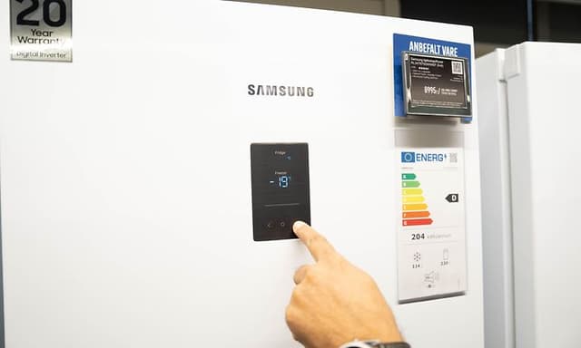 En hand som pekar på temperaturkontrollen på en frys där man ser energimärkning bredvid