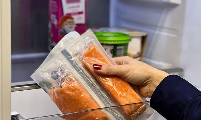 Hand holding a pack of fish in a fridge