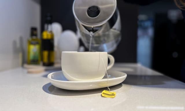 Kettle on tabletop pouring hot water into teacup