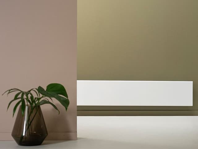 En veggmontert Adax Cleo panelradiator og grønn plante i en vase