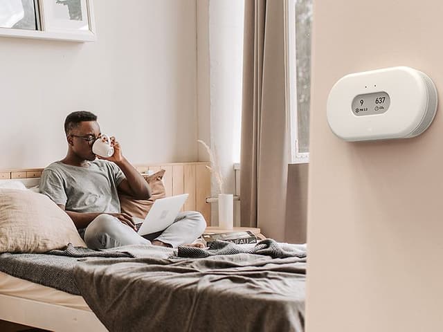 Airthings luftkvalitetsmonitor på en vegg og en mann som nyter kaffen sin