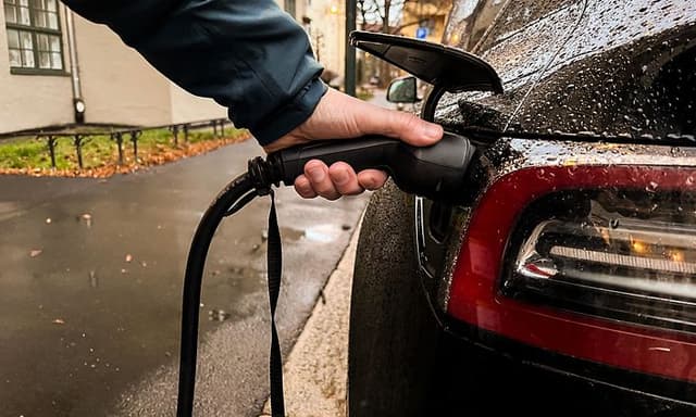 MDA - Cars and motor bikes - man plugging in a charger in a Tesla