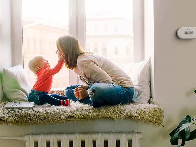 En mamma och ett barn som myser tillsammans och en Airthings luftkvalitetsmonitor på en vägg