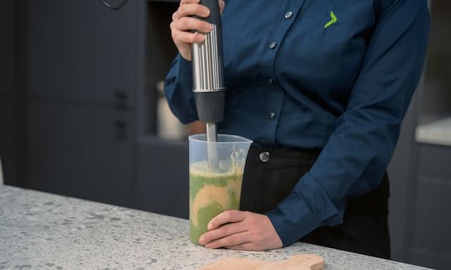 Köksapparater: Kvinnlig Elgiganten-anställd som använder en stavmixer.
