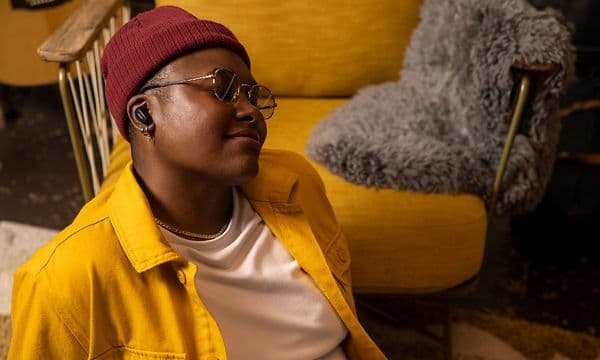 Person i en gul skjorte og rød beanie med Bose Earbuds i ørerne