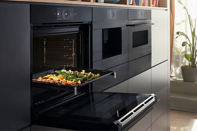 Bosch Accent line oven with the door open and a baking tray with vegetables 