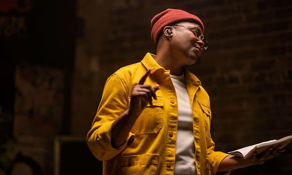 Person wearing yellow shirt and red beanie is listening with Bose Earbuds