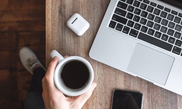 Kaffekopp på bord ved siden av bærbar PC, smarttelefon og hodetelefoner