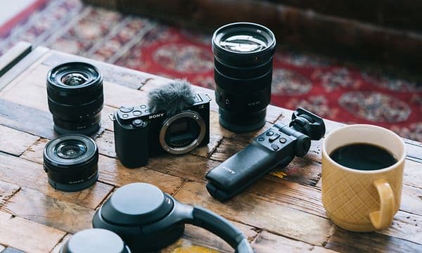 Sony ZV-E10 kamera, kaffekop og forskellige objektiver og objektiver på et bord