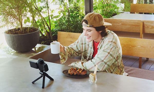 Ung mand med kaffekop i hånden, der filmer sig selv med Sony ZV-E10 kamera