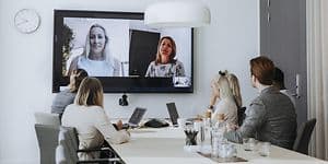 Office - B2B - people attending a hybrid meeting with laptops and a large screen