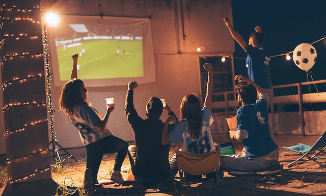 Hjemmebiograf: En gruppe venner, der ser sport på en projektor udendørs.