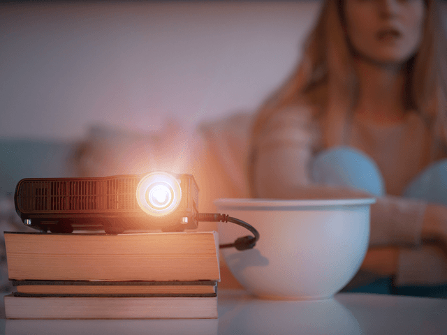 Kvinne som sitter på sofa og ser på film vist med projektor