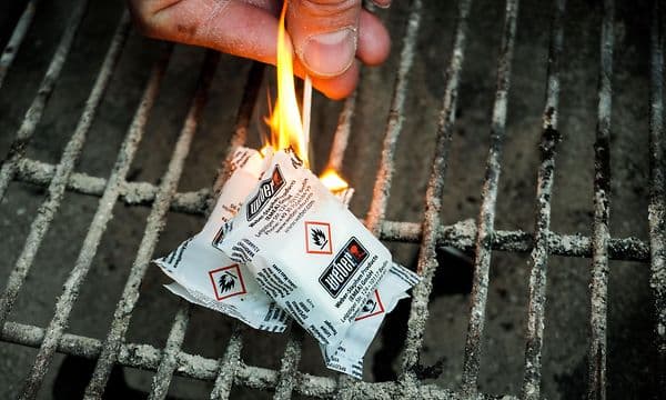 Hånd der antænder grillbriketter på en grill