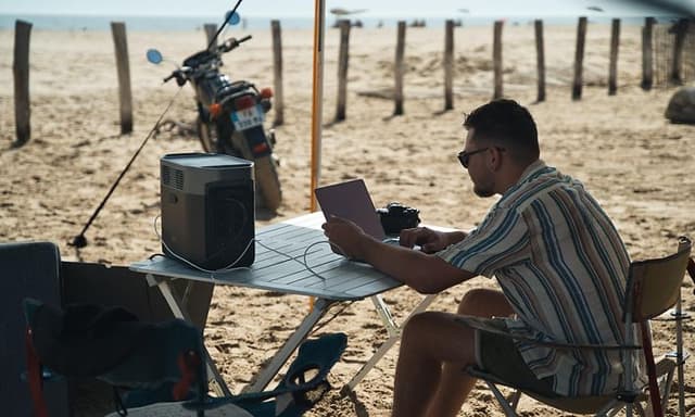 Man working on laptop on a beach with a powerstation