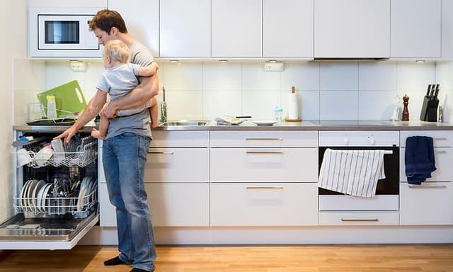 Mand der står med sit barn og fylder en opvasker med service