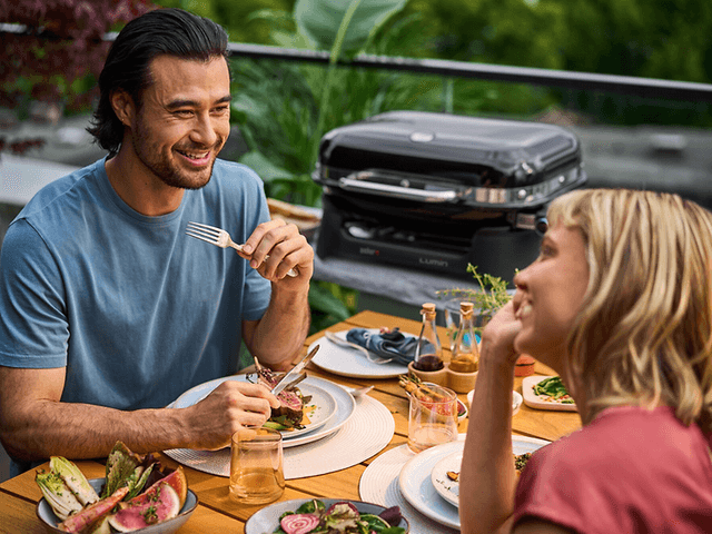 Par der spiser middag udenfor foran en grill