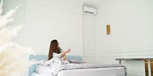 En kvinde der sidder i en seng og kontrollere en aircondition med en fjernbetjening