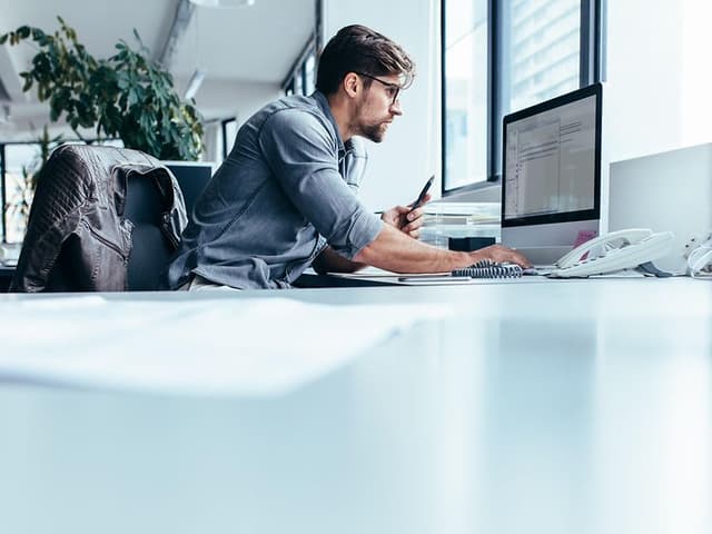 Mies työskentelee tietokoneella toimistossa